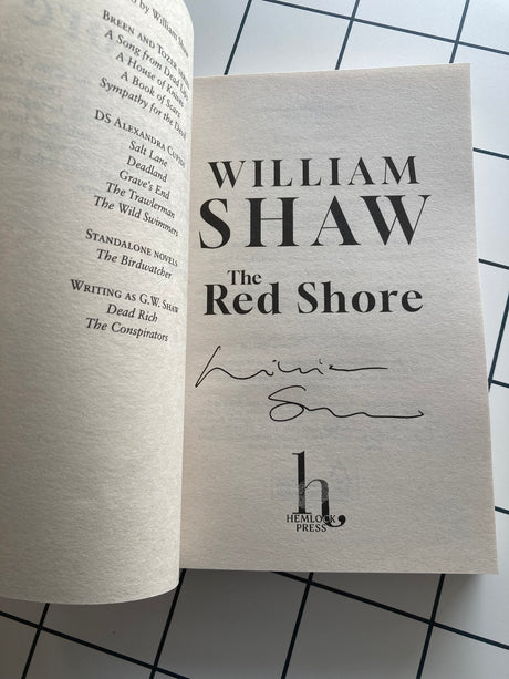 Book titled 'The Red Shore' by William Shaw with a signature on a grid background