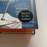 A close-up of a Susie Dent's Death Writ Large with a black circular 'Signed by the Author' sticker on the front cover.