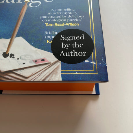 A close-up of a Susie Dent's Death Writ Large with a black circular 'Signed by the Author' sticker on the front cover.
